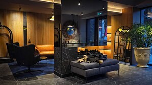 Eine moderne Lobby mit einem Ledersofa, einem schwarzen Sessel, einer Marmorbank, einer großen Topfpflanze und einem einzigartigen Wandkunstwerk.