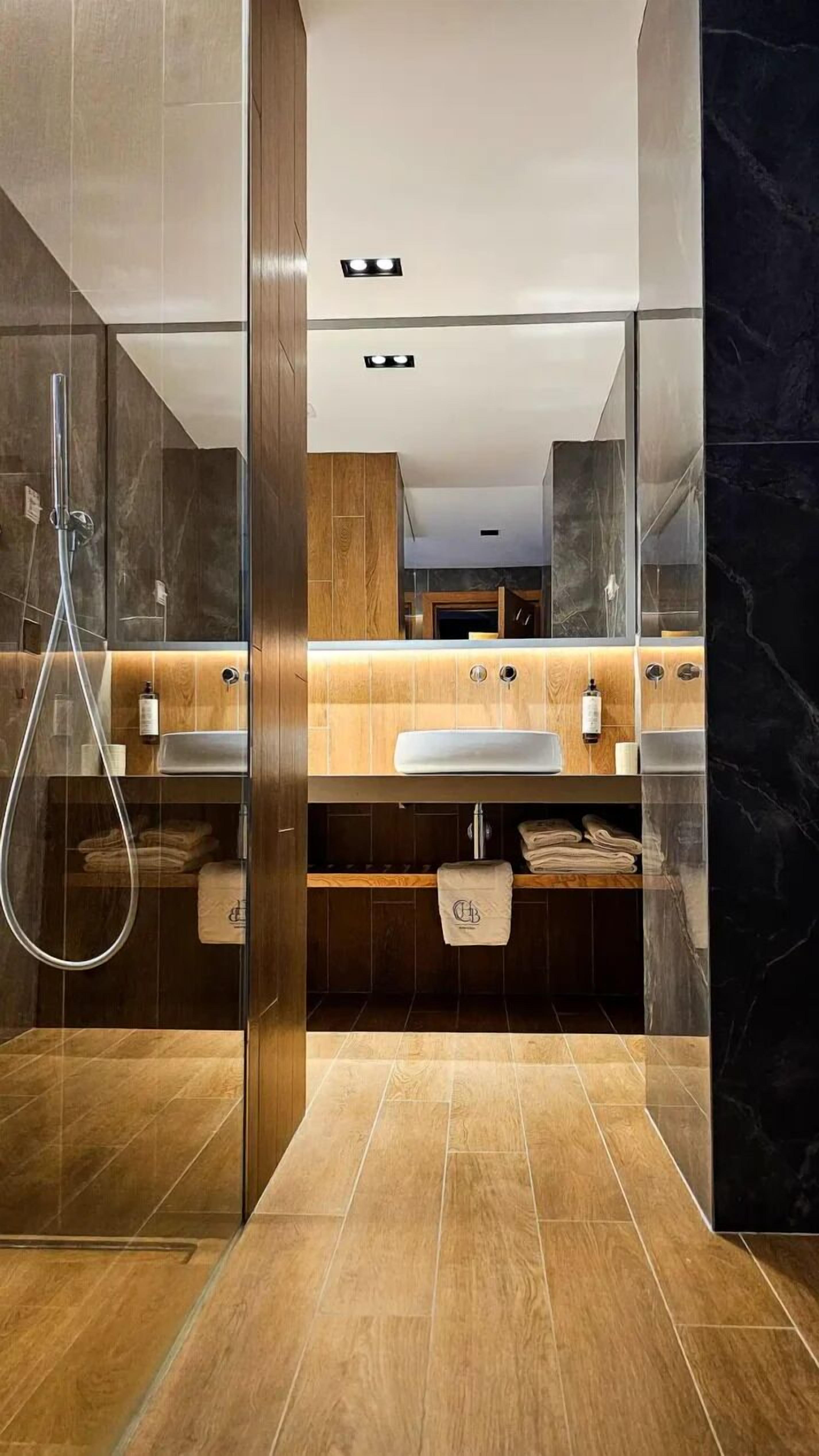 Un baño moderno con ducha de vidrio, tocador de madera y detalles de mármol.