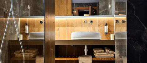 Un baño moderno con ducha de vidrio, tocador de madera y detalles de mármol.