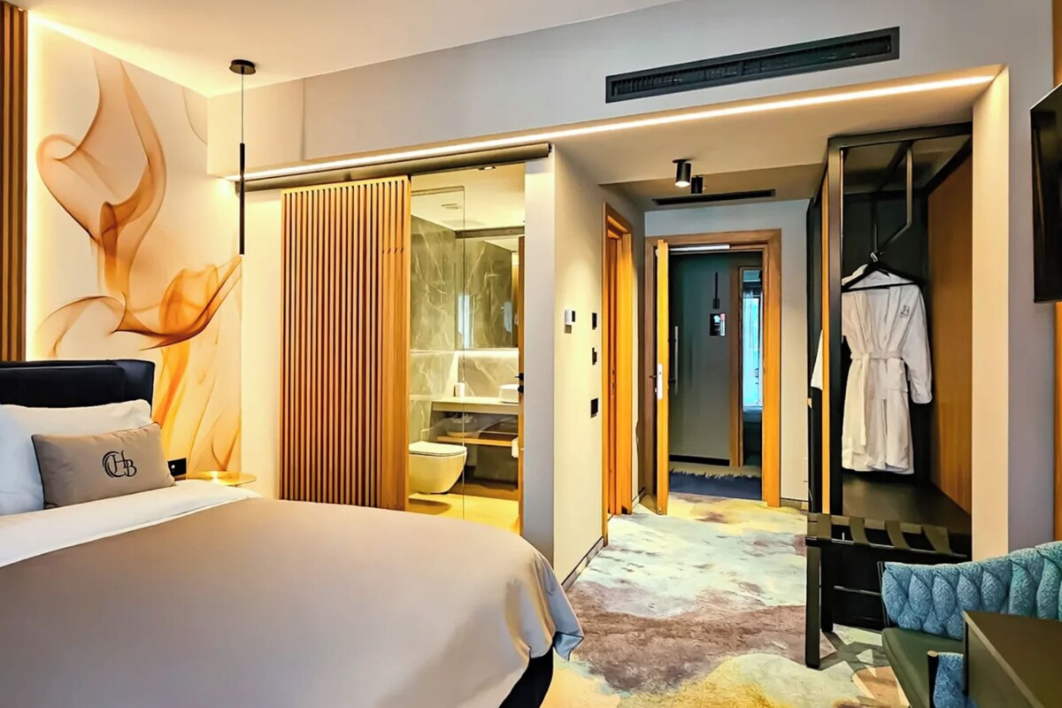 Ein modernes Hotelzimmer mit einem großen Bett, einem begehbaren Kleiderschrank und einem durch eine geöffnete Tür einsehbaren Badezimmer.