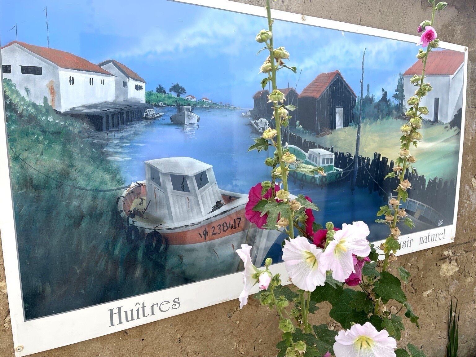 Ein gerahmtes Gemälde zeigt eine Flusslandschaft mit Booten und Gebäuden, betitelt 'Huitres'.