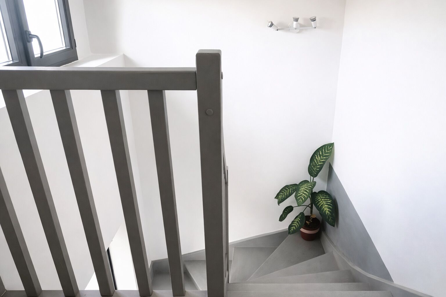 Una escalera con barandilla de madera, una planta en maceta y un aplique de pared.