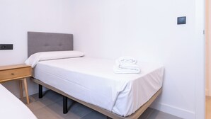 A single bed with a grey headboard, white bedding, and a folded towel on the footboard. - Beautiful apartment in the heart of Triana (Sevilla)