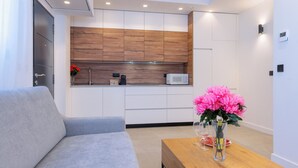 A modern kitchen with wooden cabinets, a microwave, and a coffee machine. There is a grey sofa and a wooden table with a vase of flowers. - Beautiful apartment in the heart of Triana (Sevilla)