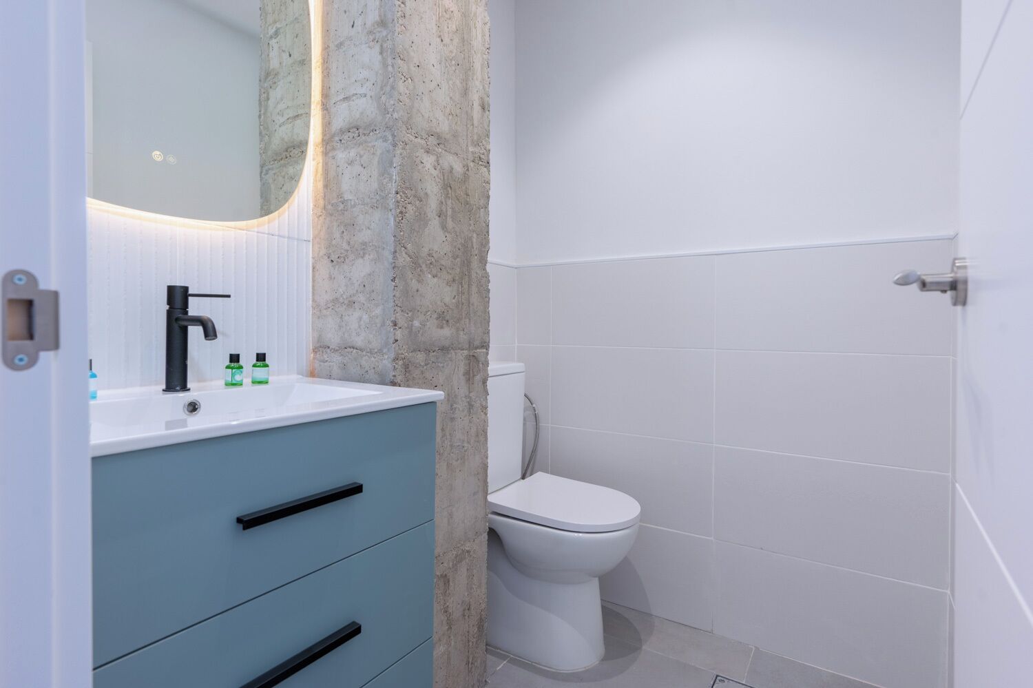 Une salle de bain avec un lavabo blanc, un meuble bleu, des toilettes blanches et un mur d’accent en pierre.