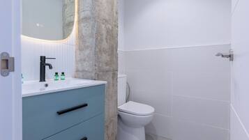 Une salle de bain avec un lavabo blanc, un meuble bleu, des toilettes blanches et un mur d’accent en pierre.