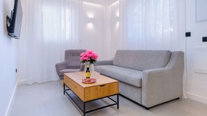 A modern living room with a grey sofa, a wooden coffee table with a bottle and glasses, and a pink flower arrangement. - Beautiful apartment in the heart of Triana (Sevilla)