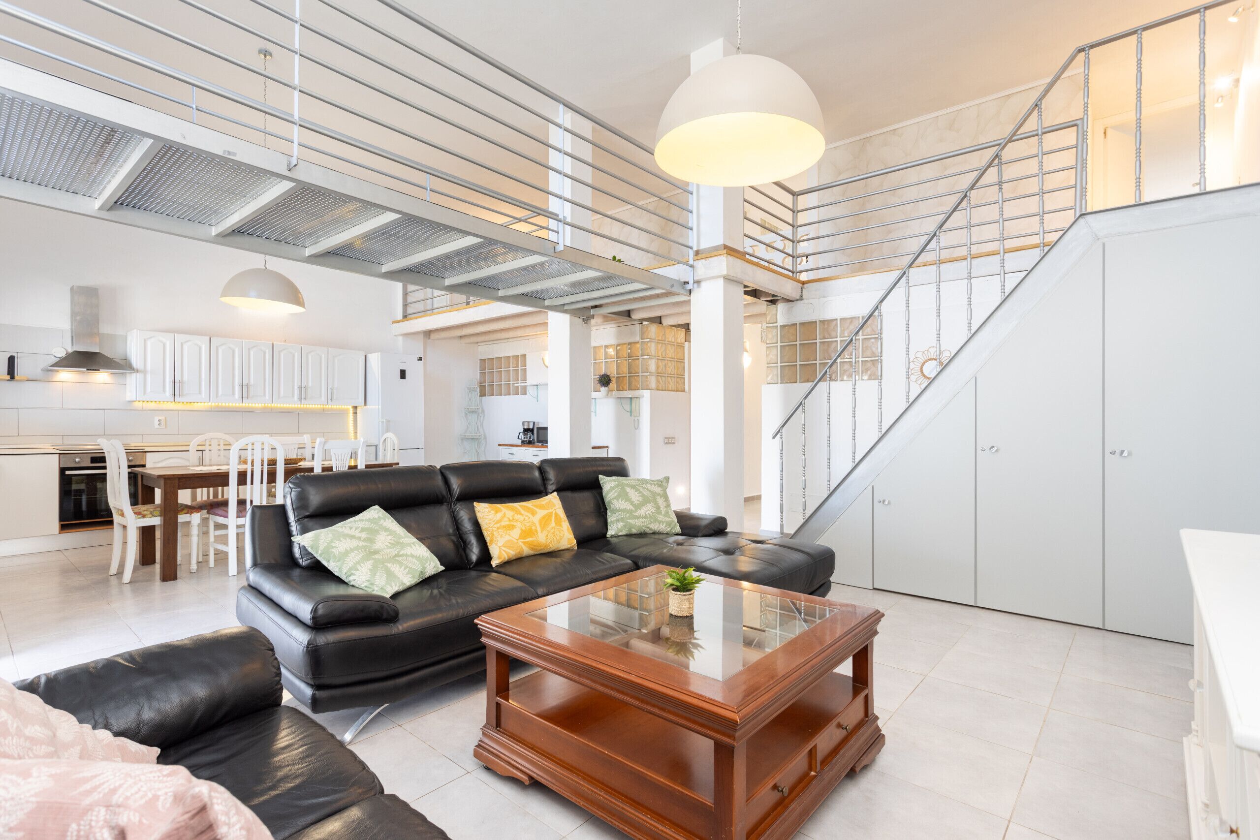 A spacious living area with a black leather sofa, a wooden coffee table, and a staircase leading to an upper level.