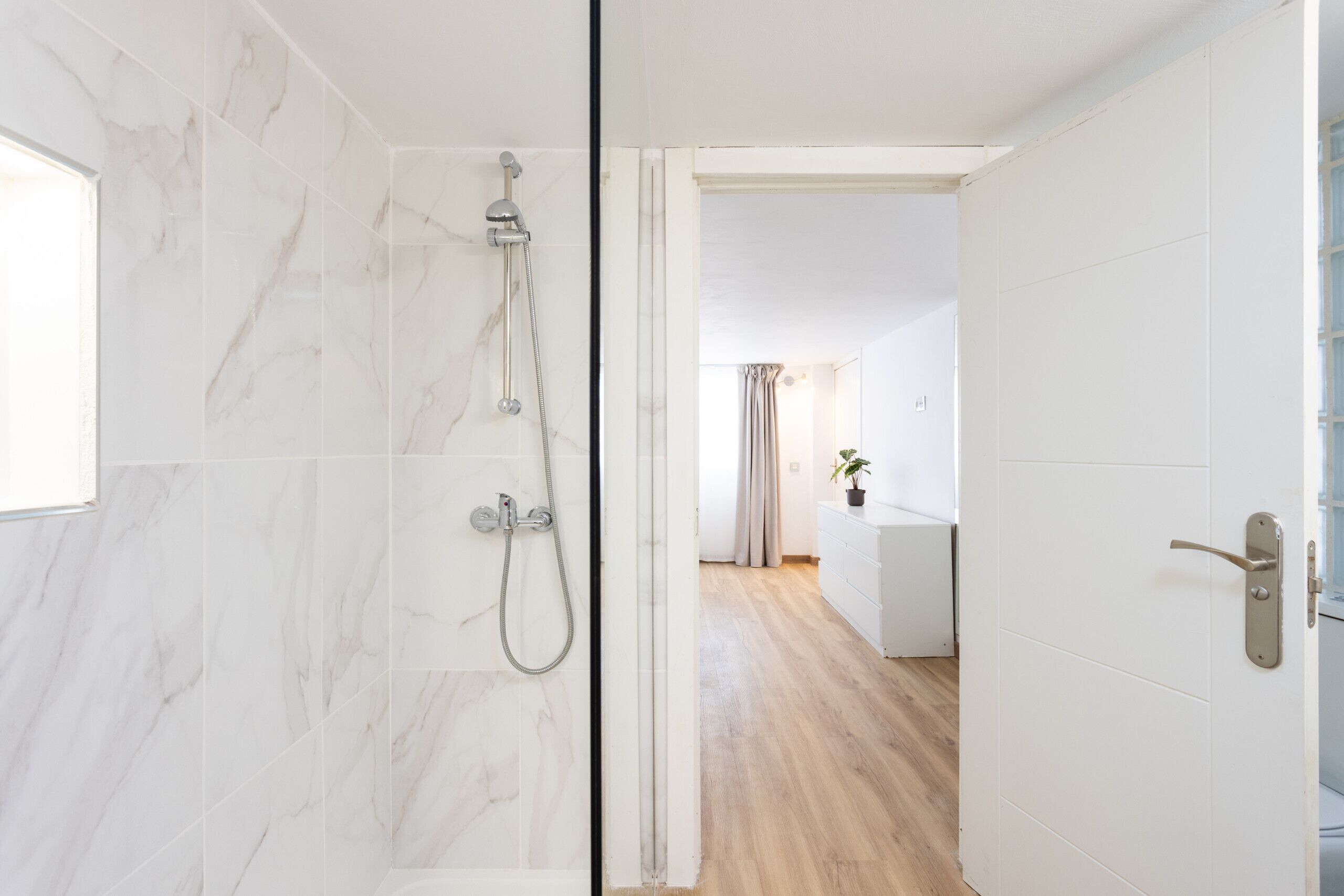 Ein modernes Badezimmer mit Dusche, Holzboden und weißer Tür.