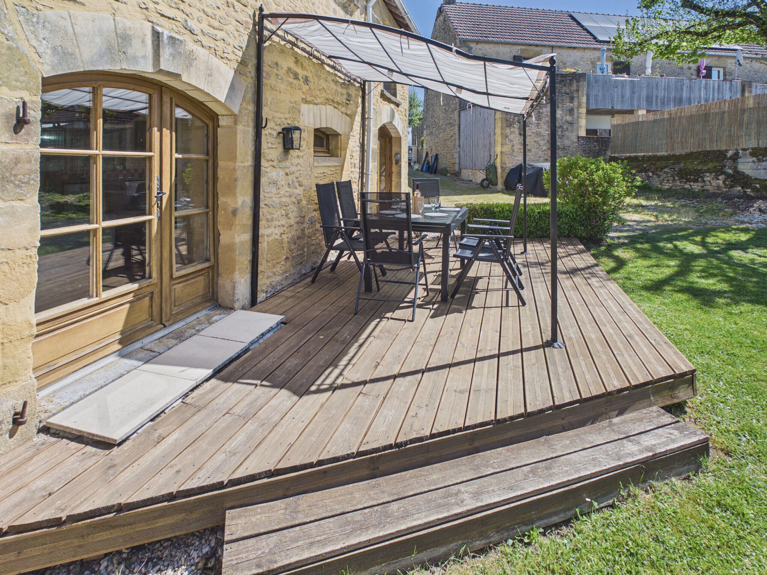 A wooden deck with outdoor furniture, a covered patio area, and a stone building with large windows.