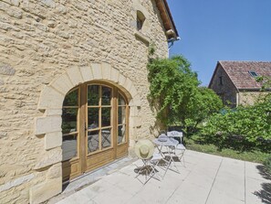 Ein Steinhaus mit einem großen Bogenfenster, Außenbereich mit Tisch und Stühlen sowie ein kleiner Garten.