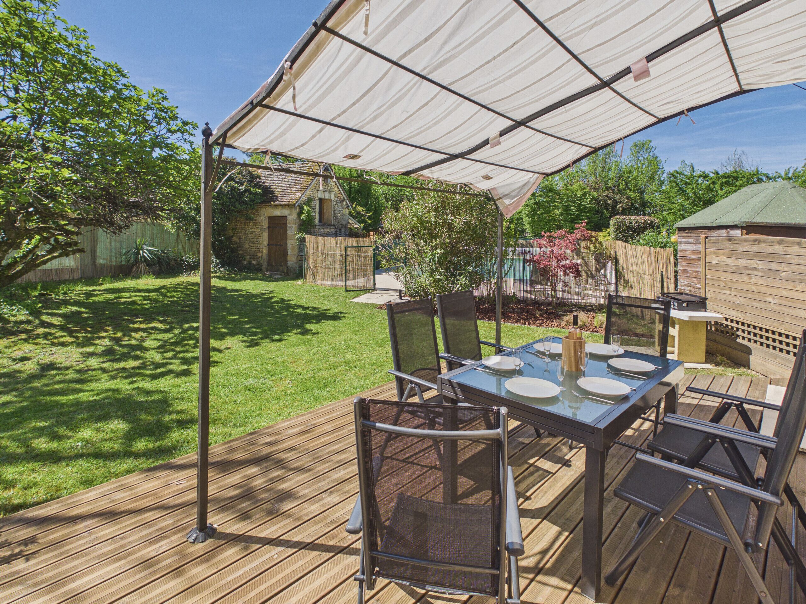 An outdoor patio with a table set for four, surrounded by chairs, under a canopy.