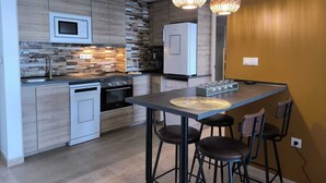 A modern kitchen with a microwave, stove, and refrigerator. There are two pendant lights, a dining table with stools, and a textured backsplash. - Mariposa de Dos Mares | Beachfront, Pool & Padel (La Manga del Mar Menor)