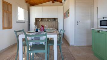 A dining area with a table set for four, chairs, a hanging light fixture, and a kitchen area with cabinets and a microwave.