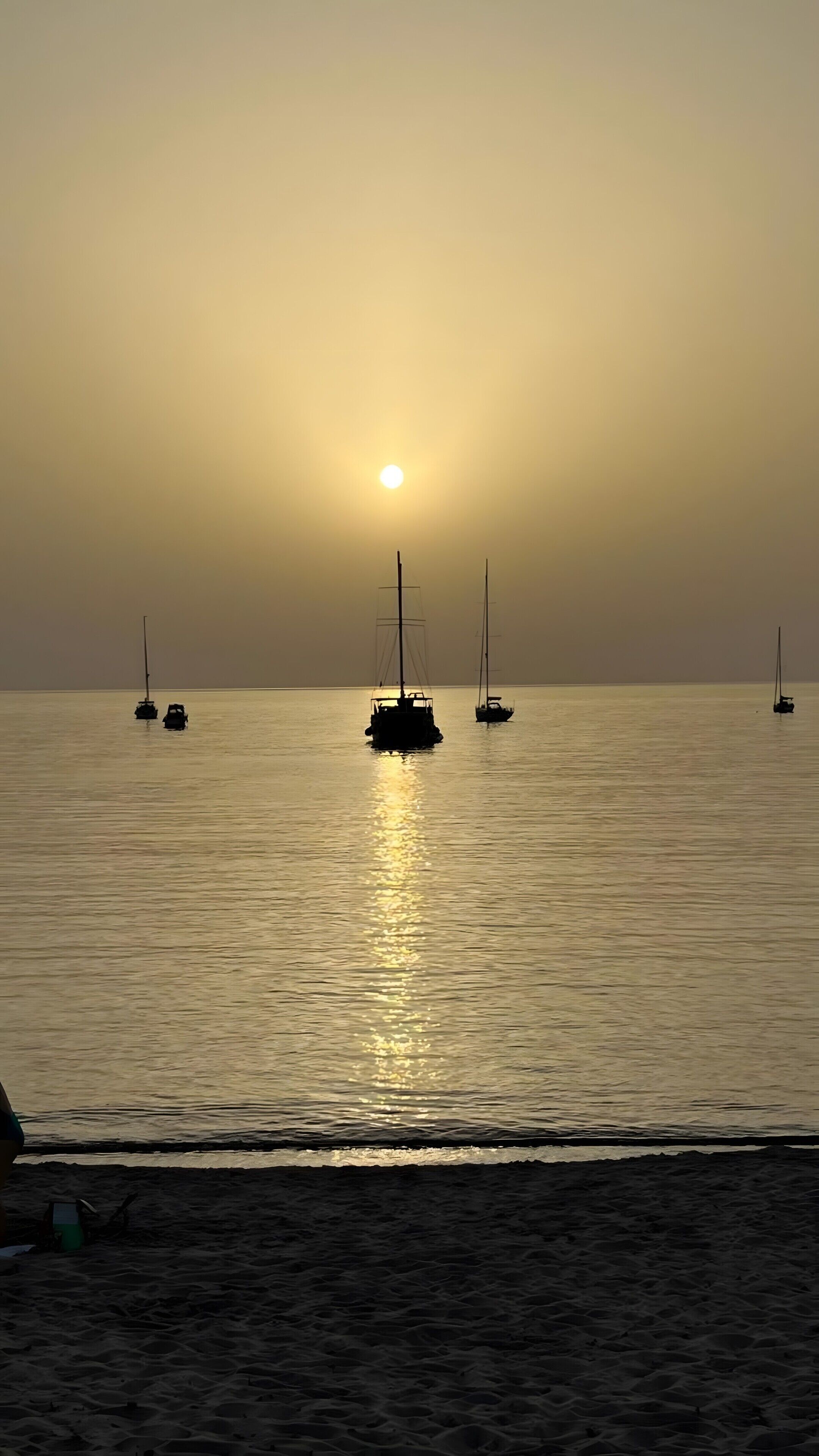 Une mer calme, avec des voiliers, au coucher du soleil.