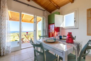 Un coin repas avec une table, des chaises, une bouilloire rouge et une vue à travers des portes vitrées.