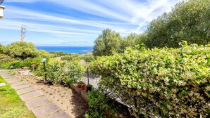 Ein Garten mit einem Kiesweg, Kübelpflanzen und Blick aufs Meer.