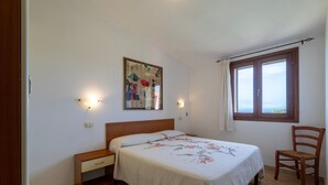 Ein Schlafzimmer mit Bett, Nachttisch, Stuhl und einem Fenster mit Vorhängen.