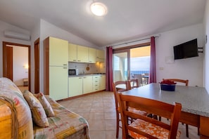 Un ambiente compatto con angolo cottura, zona pranzo e vista panoramica attraverso una porta vetrata.