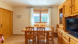 A dining area with a wooden table and chairs, a TV on a wooden cabinet, and a window with curtains. - Holiday Home Paraíso Ground Floor - Lake Views, Gredos & Garden (Ávila)