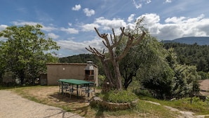 A rustic outdoor dining area with a table and chairs, a small building with a chimney, and a tree in the foreground. - Holiday Home Paraíso Ground Floor - Lake Views, Gredos & Garden (Ávila)