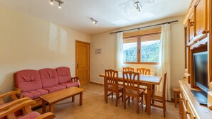A living room with a sofa, wooden chairs, a dining table, a TV, and a window with curtains. - Holiday Home Paraíso Ground Floor - Lake Views, Gredos & Garden (Ávila)