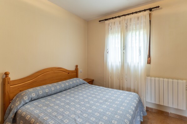 A bedroom with a wooden bed, a nightstand, a radiator, and a window with curtains.