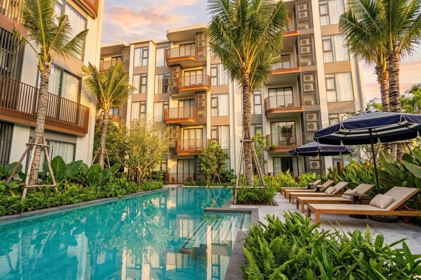 Um hotel moderno com piscina, espreguiçadeiras e palmeiras.