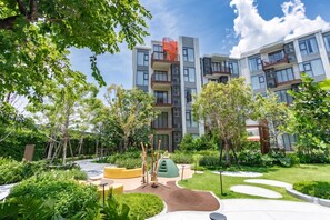 Um edifício de apartamentos moderno com varandas, área de recreação infantil e vegetação ao redor.