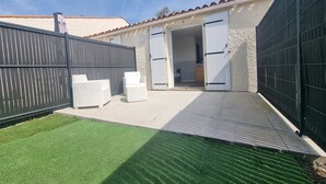 Un jardín trasero con césped artificial, un patio y una zona de estar exterior blanca.