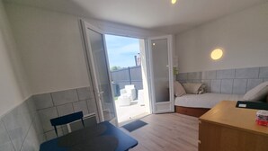 Habitación pequeña con cama, una mesita y una silla. Cuenta con una puerta corredera que da a un espacio al aire libre.
