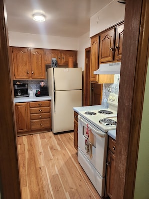 A kitchen with wooden cabinets, a refrigerator, a stove, and a coffee maker.