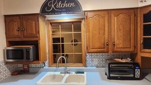 A kitchen with wooden cabinets, a microwave, a toaster, a sink, and a window with a grid pattern. - Charming 2-bedroom apartment with AC in vibrant Austin,Mn (Austin)