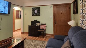 A living room with a television, wooden furniture, a clock, and a door. - Charming 2-bedroom apartment with AC in vibrant Austin,Mn (Austin)