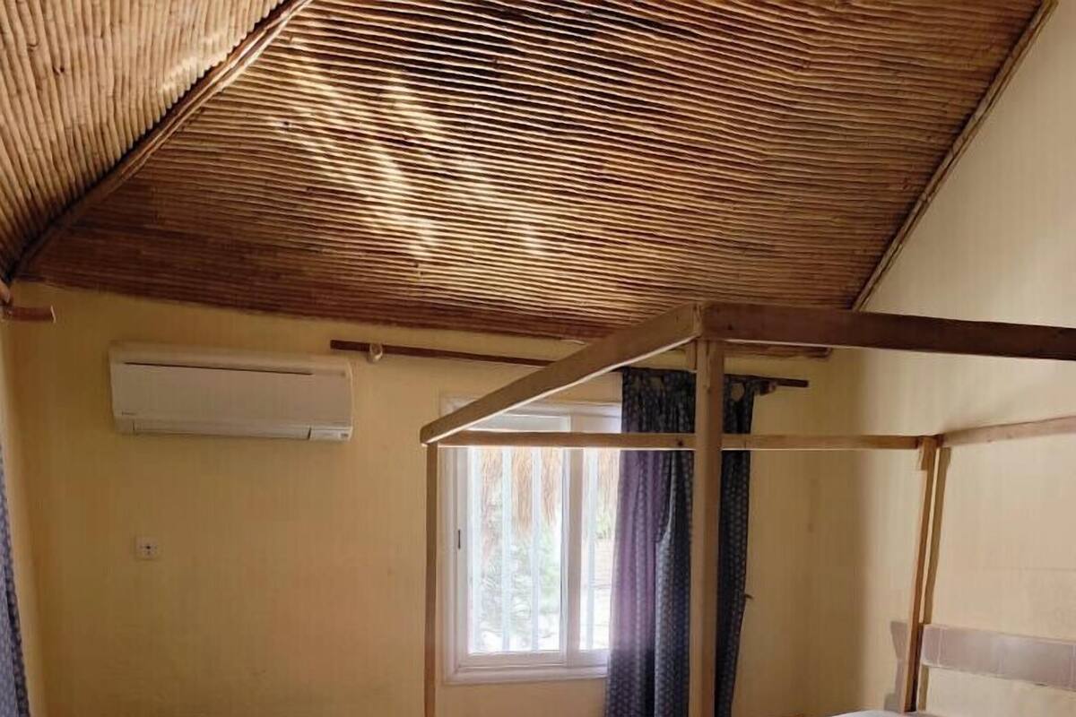 A single bed with a wooden frame, a desk with a chair, and a window with curtains.