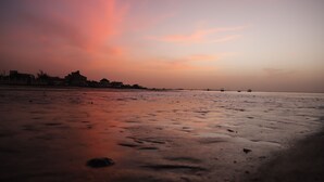 A beach with a sunset sky, calm water, and distant buildings. - A La Teranga (Foundiougne)