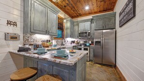 A kitchen with wooden cabinets, a central island, bar stools, a microwave, and a refrigerator. - 2BR Family Retreat with Bunk Room and Hot Tub (Broken Bow)