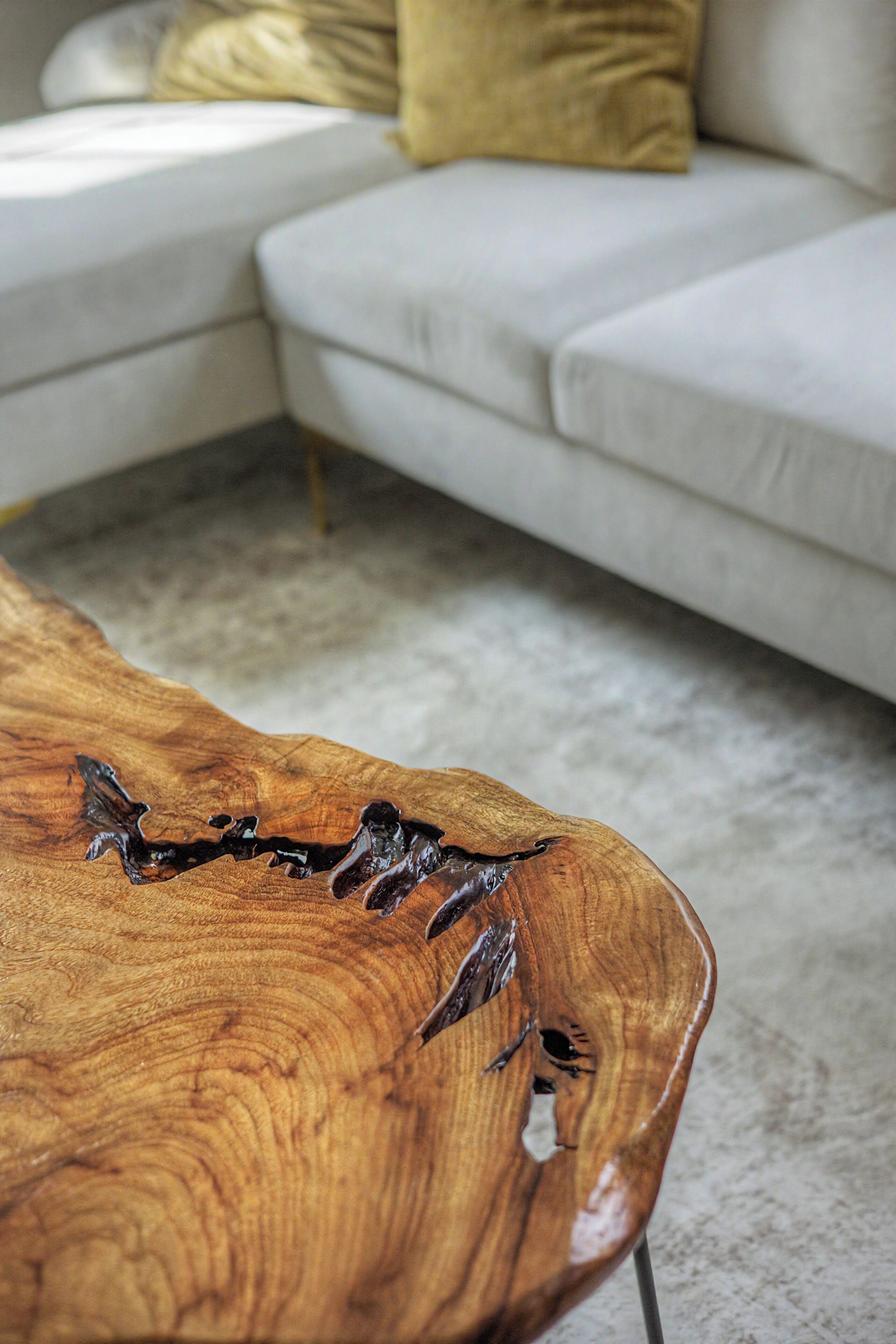 Un tavolino da caffè in legno dal design originale, un divano bianco con cuscini gialli e un pavimento rivestito di tappeto.
