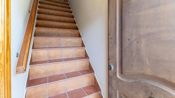 Una scala con piastrelle in terracotta, ringhiera in legno e una porta di legno.