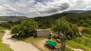 Paesaggio rurale con un sentiero sterrato, un piccolo edificio con tetto in tegole e un tavolo verde con sedie.