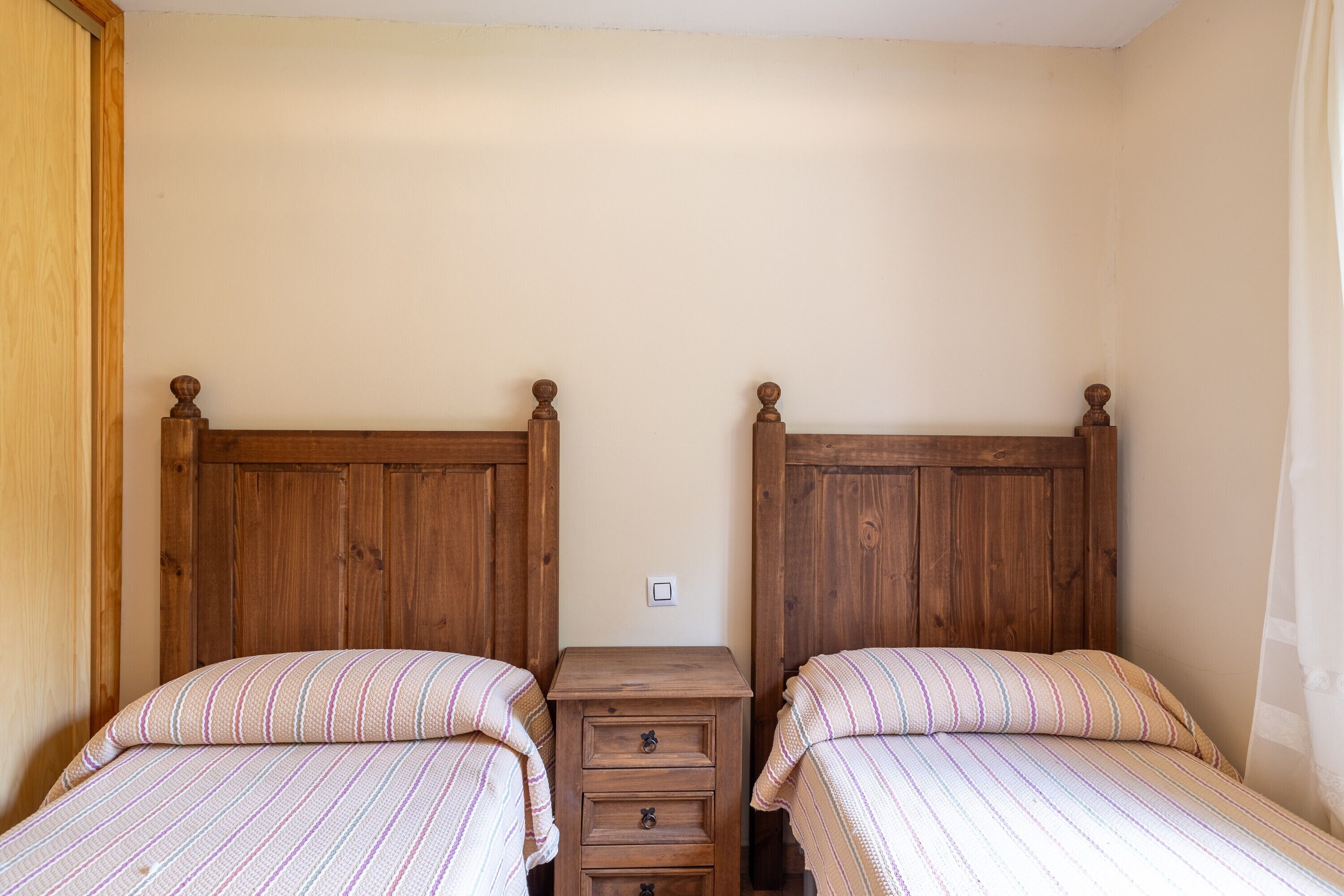 Ein Schlafzimmer mit zwei hölzernen Betten, einem kleinen Nachttisch dazwischen und einer schlichten Wand.