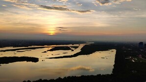 Een zonsondergang boven een groot wateroppervlak, met een stadsgezicht op de achtergrond.