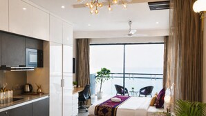 Een moderne hotelkamer met een balkon, een kitchenette, een bed met een decoratief hoofdeinde en een zithoek met uitzicht.