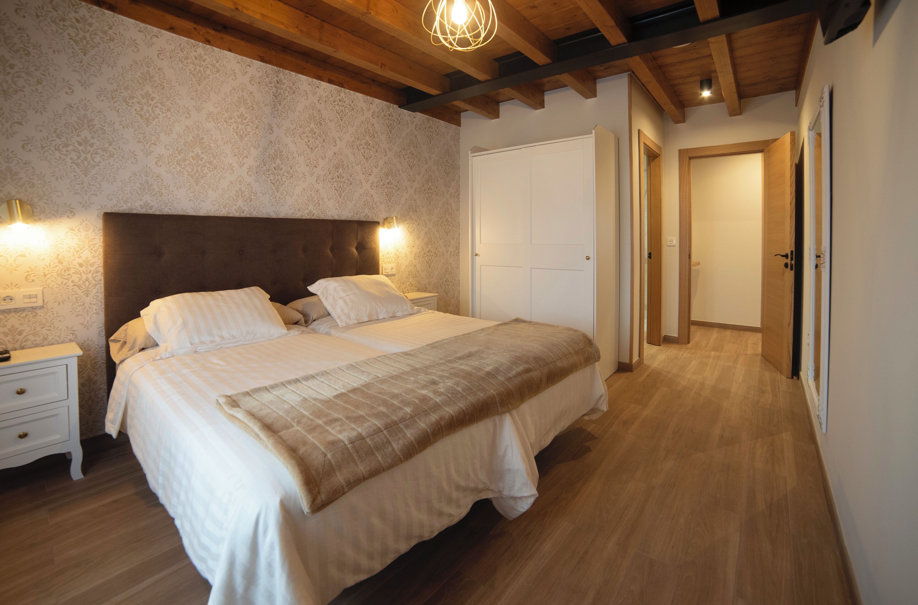 A bedroom with a large bed, wooden headboard, and a nightstand with a lamp.