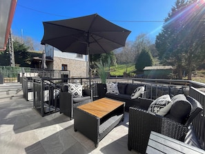 An outdoor patio with wicker furniture, a wooden table, and a large umbrella. - Spectacular apartment in the Picos de Europa, Asturias. Natural Paradise. (Onis)