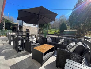 Un área de patio al aire libre con muebles de mimbre, una mesa de madera y una sombrilla grande.
