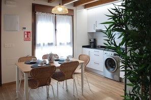 Una cocina pequeña y limpia con lavadora, una mesa de comedor con sillas y un ventanal con cortinas.