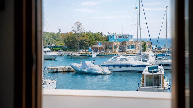 Un puerto deportivo con barcos amarrados, un edificio de fachada azul y una estructura de piedra.