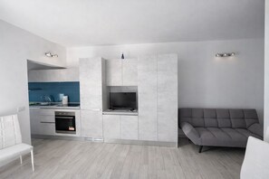 Moderni keittiö, jossa on integroidut kodinkoneet, harmaa sohva ja valkoinen penkki.