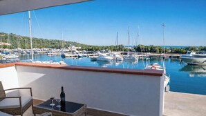 Un balcón con vista a un puerto deportivo, una botella de vino y una copa sobre una mesa.